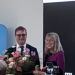Two smiling individuals hold a bouquet, celebrating the documentary "This is the Work" about Esther Wojcicki.