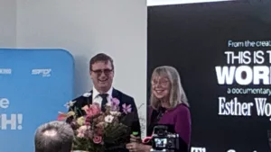 Two smiling individuals hold a bouquet, celebrating the documentary "This is the Work" about Esther Wojcicki.